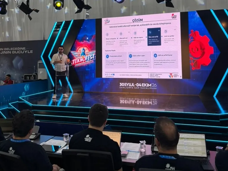 Osman Yağmur sahnede AlphaAnalytica'nın çözümünü sunuyor; arkasındaki büyük ekranda sunum, önde jüri üyeleri.